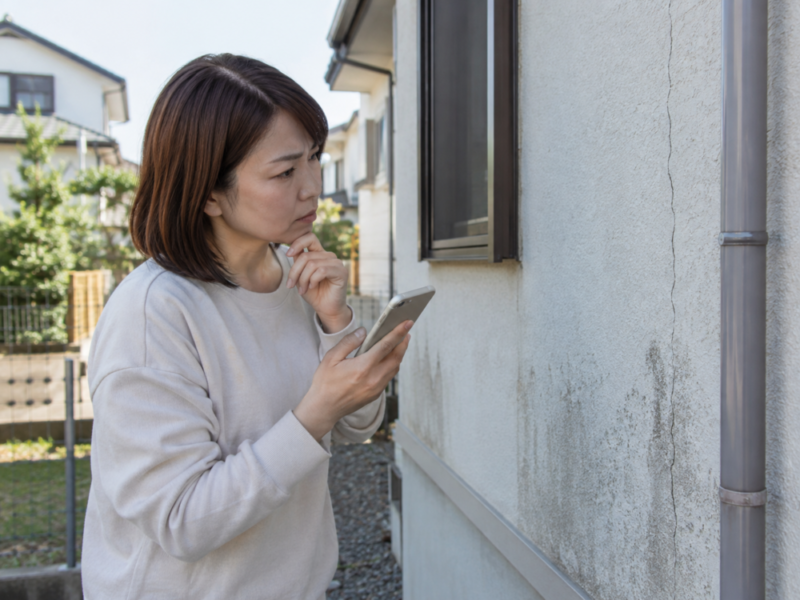 外壁のひび割れをスマートフォンで確認する女性